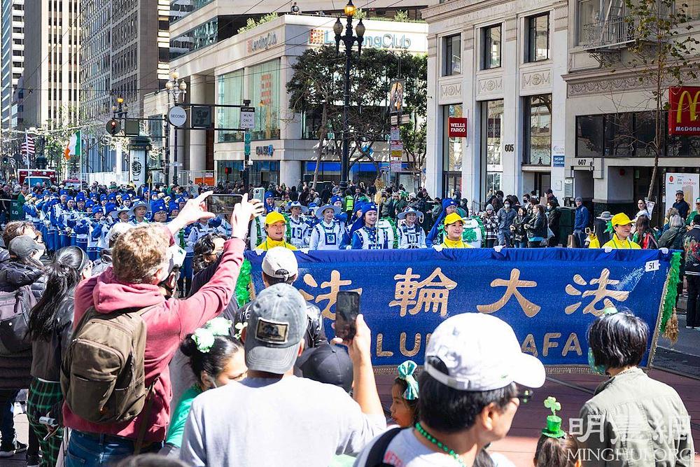 Gledatelji su pozdravili Falun Dafa praktikante klicanjem, a mnogi su snimali glazbu Tian Guo Marching Banda