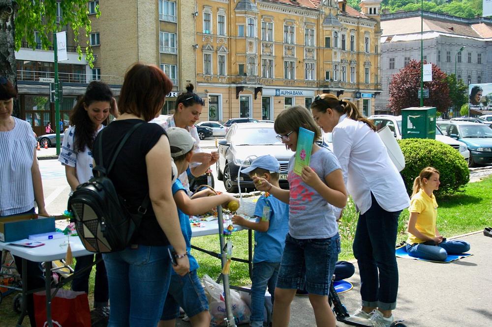 Na štandu Latice Mira nuđeni su origami cvetovi i uputstva kako ih napraviti. Praktikantkinja pored radi meditaciju Falun Dafe  